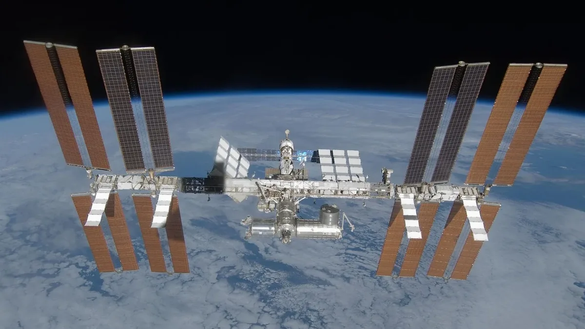 The International Space Station (ISS) in orbit around Earth, with solar panels and other equipment visible.