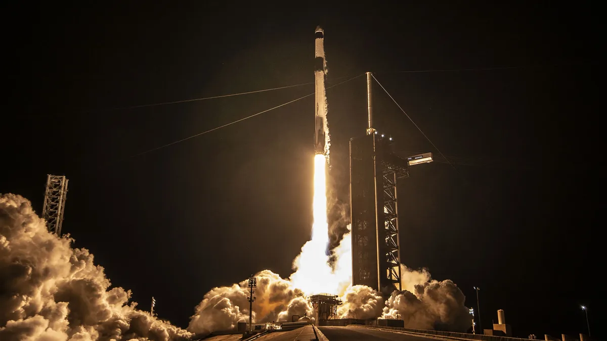 A rocket launch, with the rocket situated on a launchpad, emitting a large plume of smoke and flames as it ascends into the sky.
